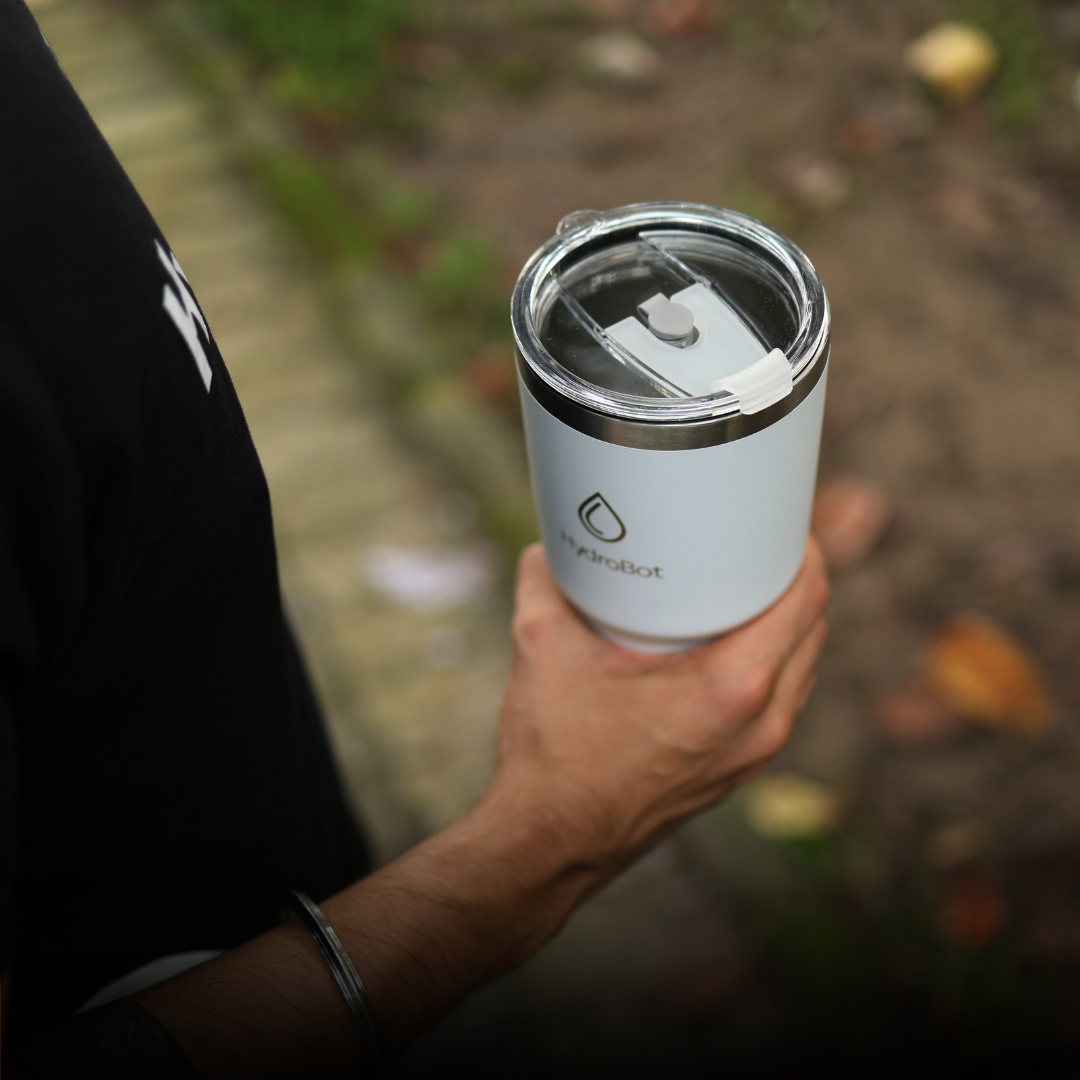Close-up of a coffee filter and a black kettle on a table with people in the background.